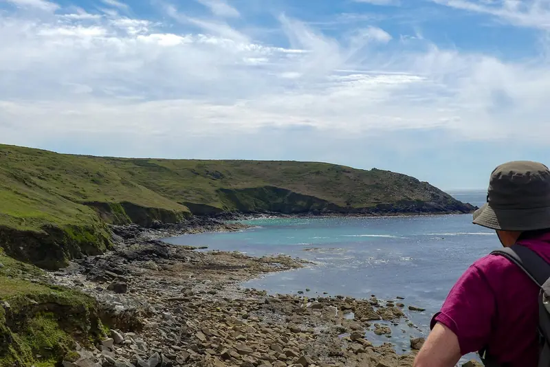 Hiker overlooking a turquoise cove along the Cornwall coastline