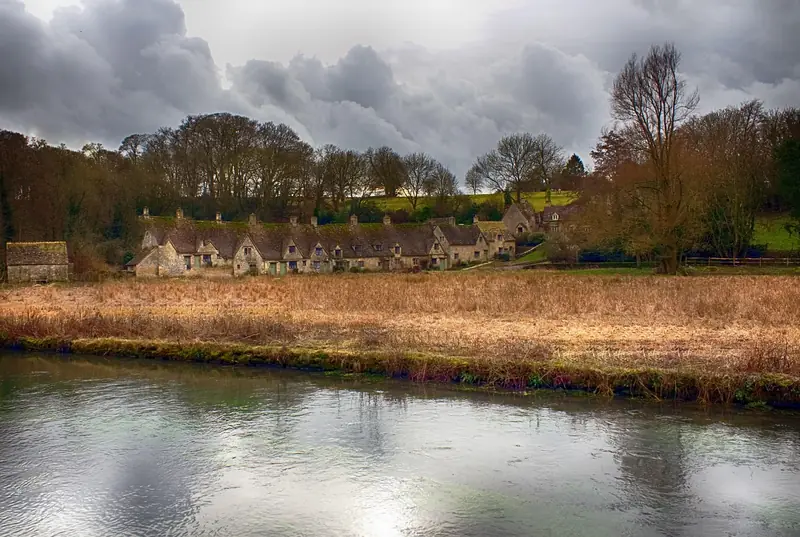 Row of honey-coloured stone cottages beside a river in the Cotswolds