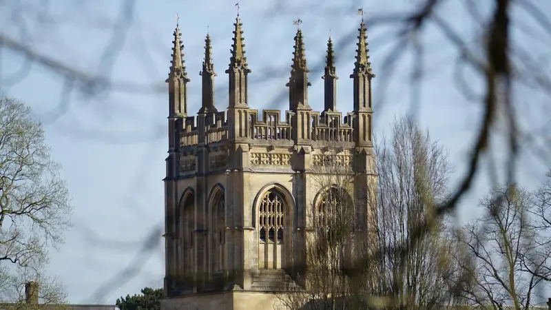 Gothic spires of an Oxford University college framed by bare tree branches